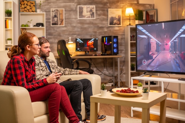 Couple playing video games on big screen TV in the living room late at night.