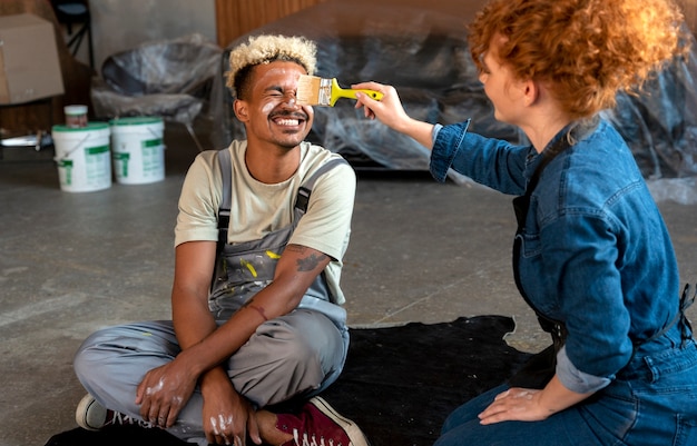 Couple posing together in their new home while holding paintbrush