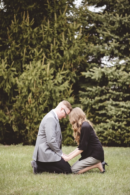 A couple praying together on their knees on a grassy lawn with trees in the background