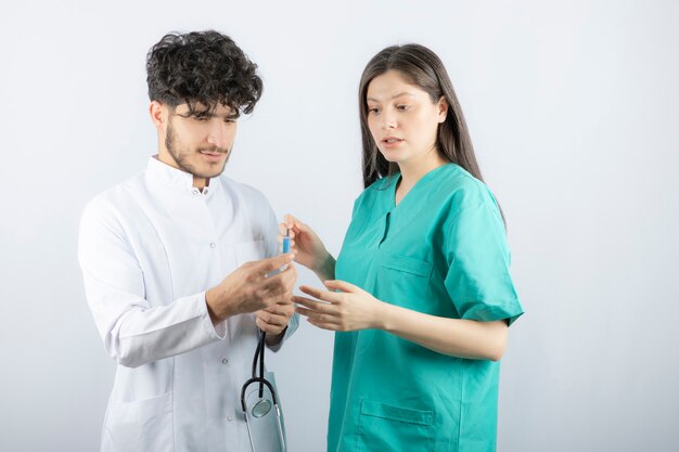 Couple of professional doctors looking at syringe on white. 