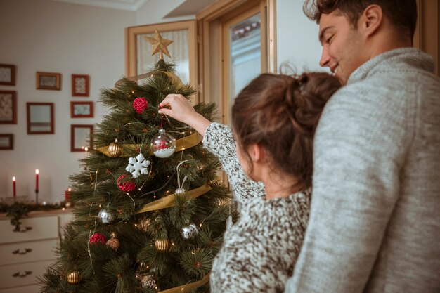 Couple putting baubles on Christmas tree 