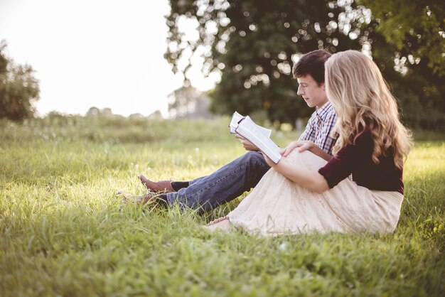 日光の下で庭で一緒に聖書を読んでいるカップル