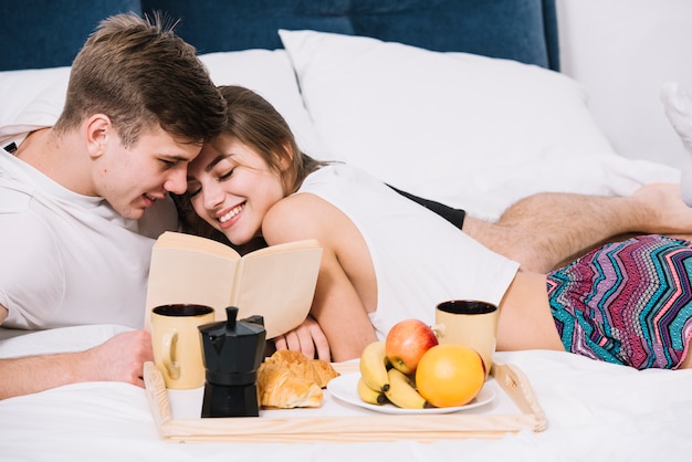 Free photo couple reading book on bed with tray of food