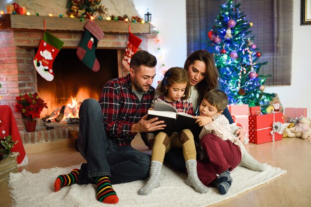 Couple reading a book with children in their living room decorated for christmas