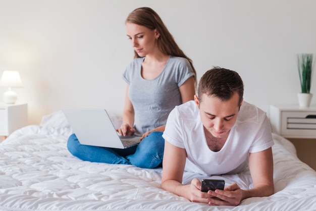 Couple relaxing on bed with devices