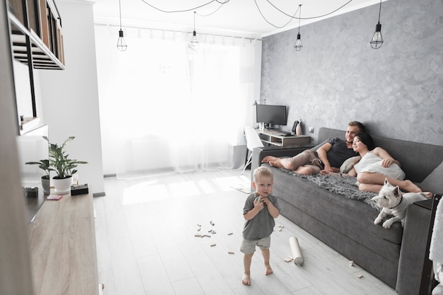 Couple relaxing on sofa with dog and their son playing with toys at home