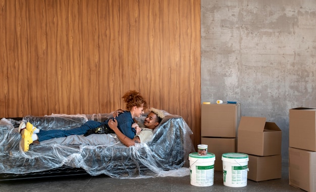 Free photo couple resting on a sofa in their new home next to paint buckets