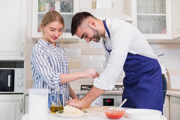 Couple rolling dough for pizza at table 