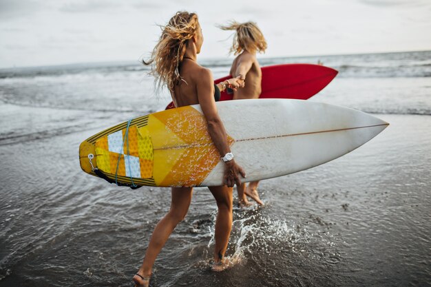 Couple runs along coast to sea. Man and woman are going to surf