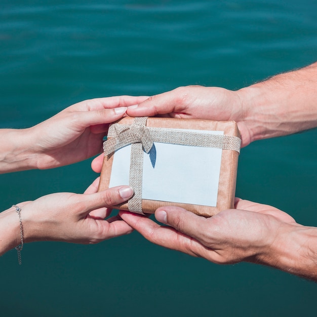 海の水の背景に贈り物をしているカップルの手