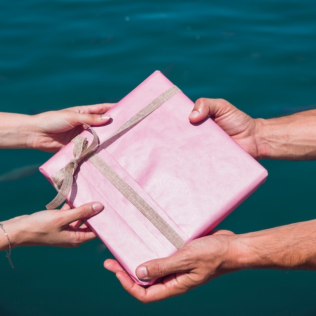 Free photo couple's hand holding gift in front of sea