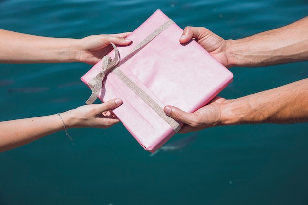 커플의 손을 잡고 바다 물 배경 앞에서 분홍색 선물 상자