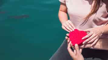 Free photo couple's hand holding red heart shape near sea