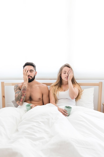 Couple sitting on bed covering their one eye