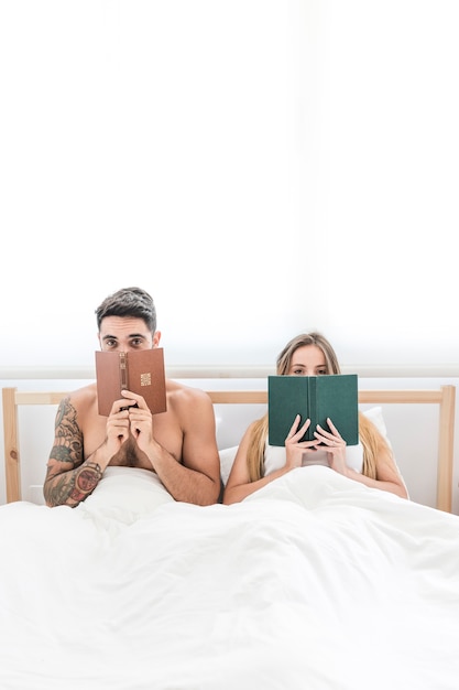 Couple sitting on bed peeking from book