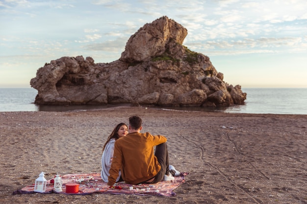 Coppie che si siedono sul coverlet sulla riva di mare