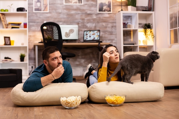 Couple sitting on the floor and watching TV in their living room.