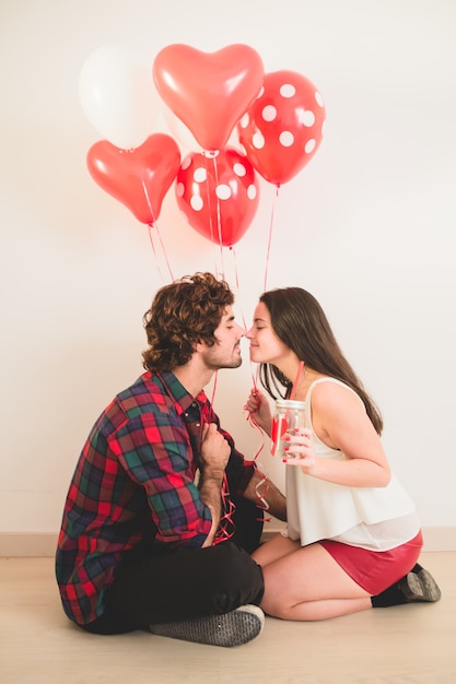 Couple sitting on the floor with balloons in hand nose with nose
