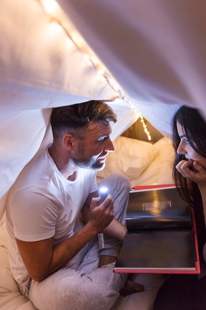 Couple sitting inside the bed under the curtain looking at magazine