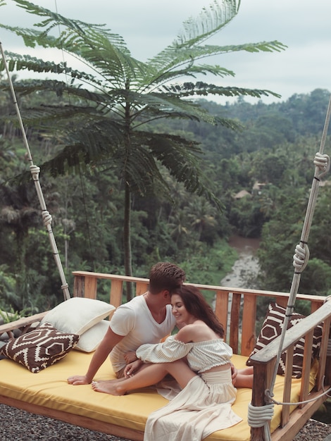 Free photo couple sitting on a large swing on a bali