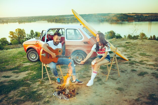 Couple sitting and resting on beach playing guitar on a summer day near river