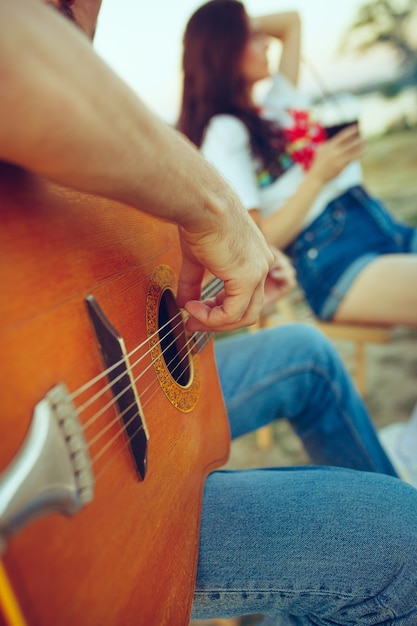 Couple sitting and resting on beach playing guitar on a summer day near river