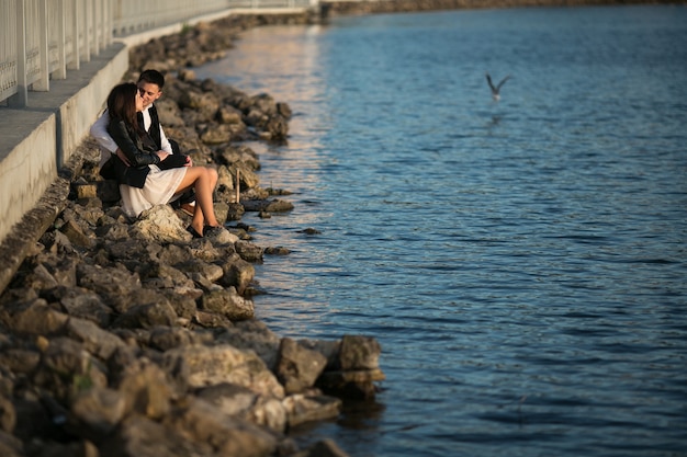 Free photo couple sitting on the rocks by the sea