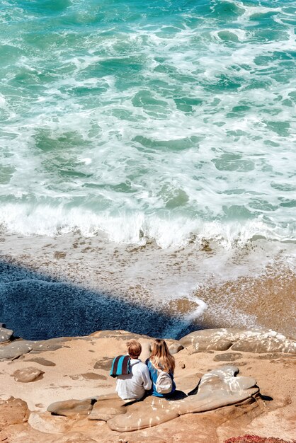 岩の上に座って、アメリカのサンディエゴの海を見ているカップル