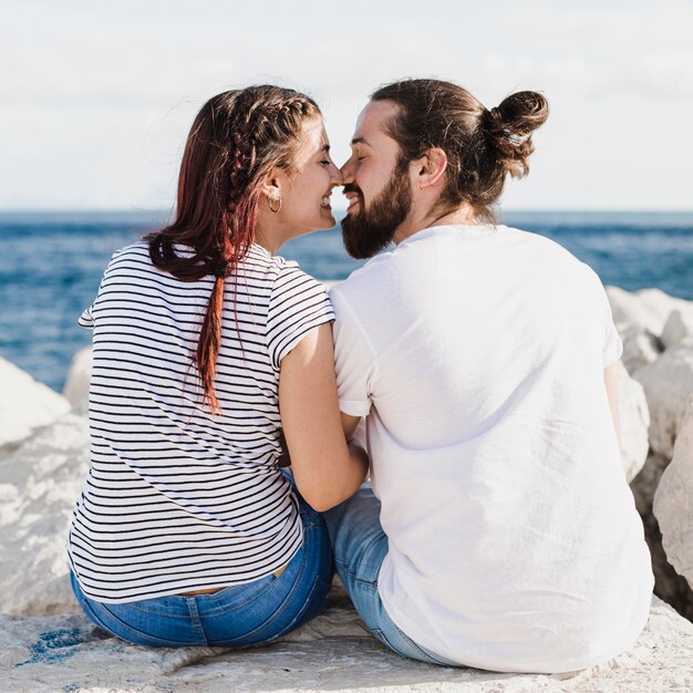 海で岩の上に座ってキスをしているカップル