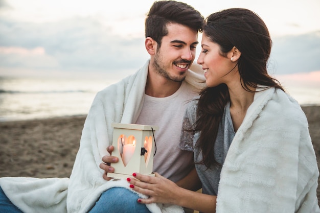 Free photo couple sitting on the sand with a candle and a blanket