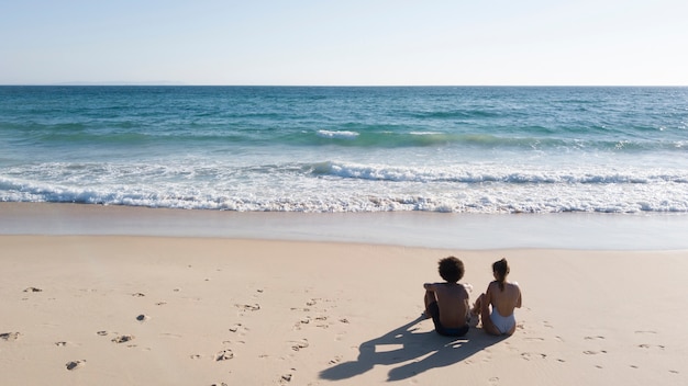 Free photo couple sitting on sandy beach