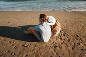 Free photo couple sitting next to the sea leaning against each other