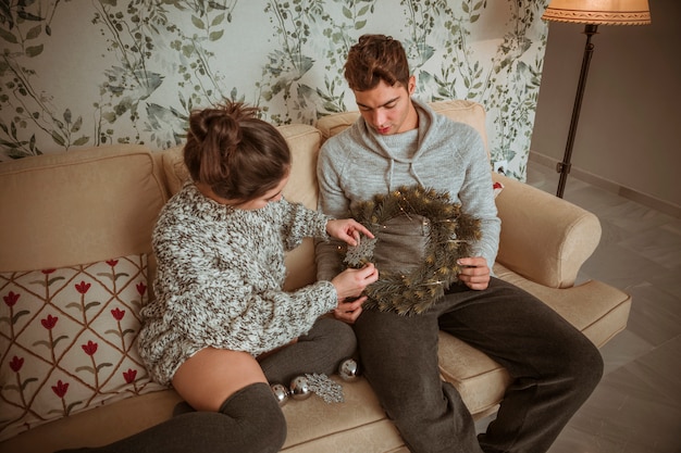 Couple sitting on sofa decorating Christmas wreath