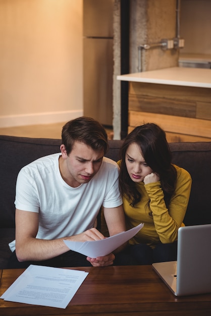 Couple sitting on sofa discussing with financial documents in living room