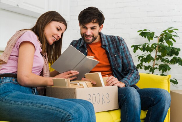 Free photo couple sitting on sofa reading book with box in the living room