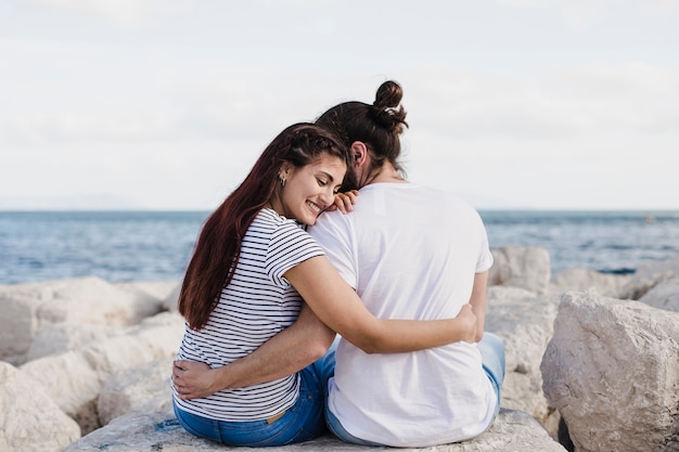 Free photo couple sitting together on rocks at the sea