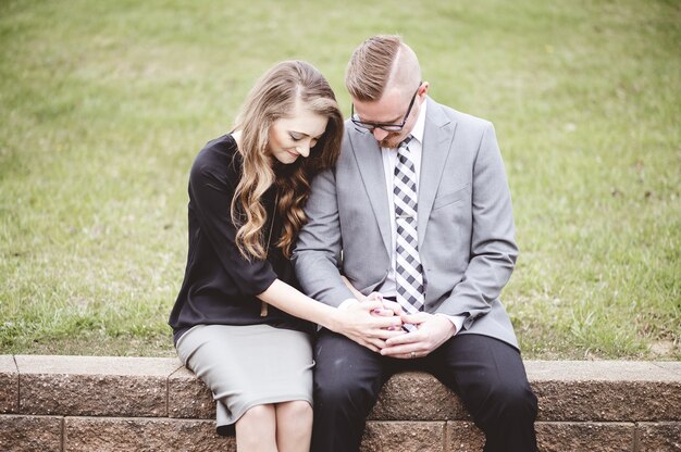 Couple sitting while holding hands together and praying beside a grassy lawn