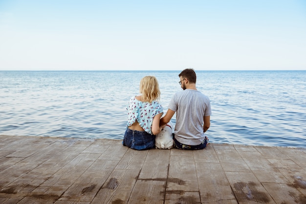 Couple sitting with French bulldog near sea