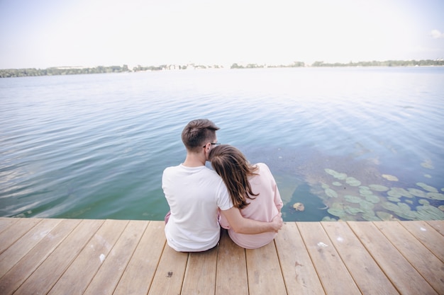 Couple sitting on a wooden pier and her head resting on the shoulder of him