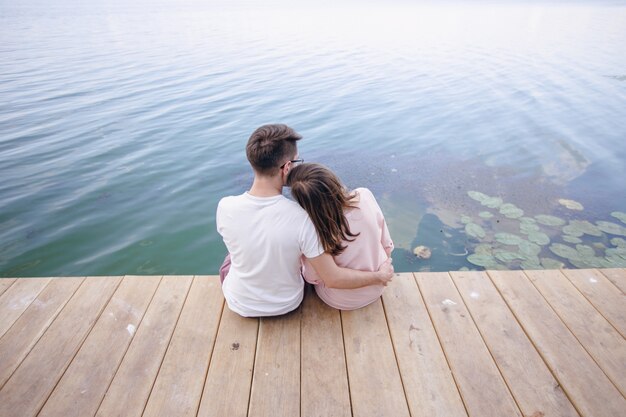 Couple sitting on a wooden pier and her head resting on the shoulder of him