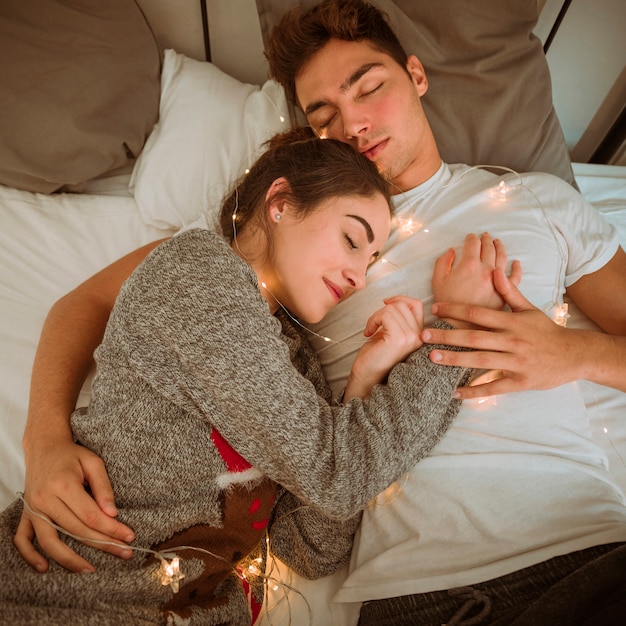 Free photo couple sleeping on bed with garland