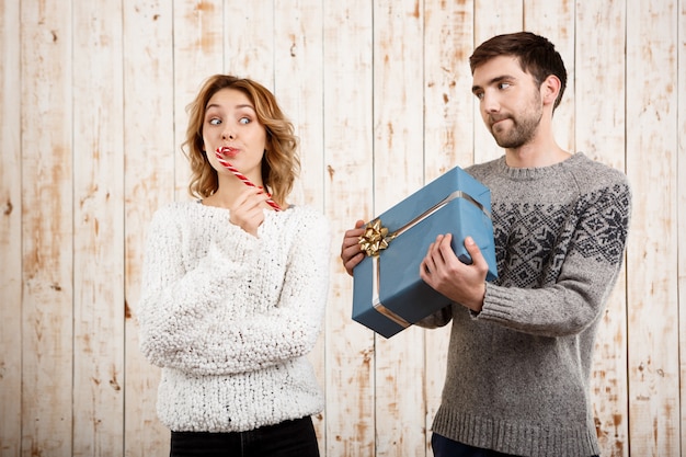 Free photo couple smiling holding christmas candy and gift over wooden wall