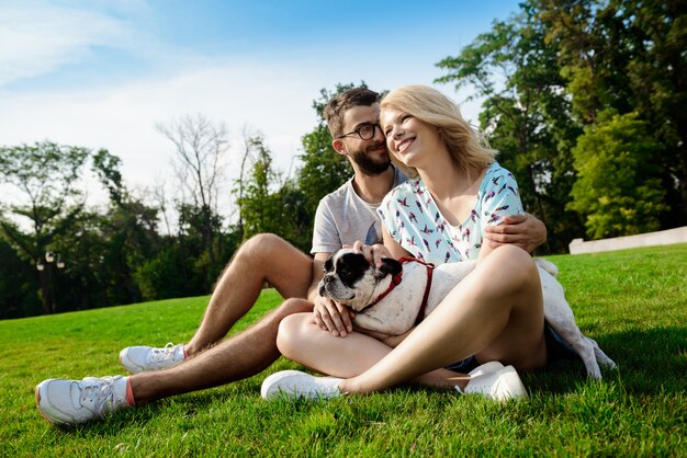 笑みを浮かべて、公園でフレンチブルドッグと草の上に座ってカップル