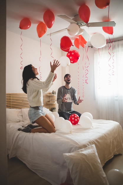 Couple smiling with hands raised looking at the ceiling full of heart shaped balloons