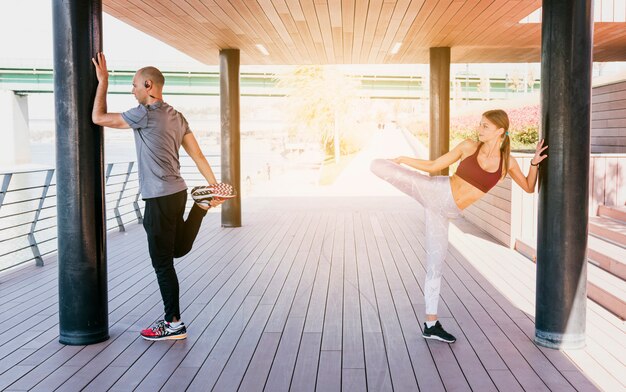 Couple standing near the pillar stretching her leg while doing exercise