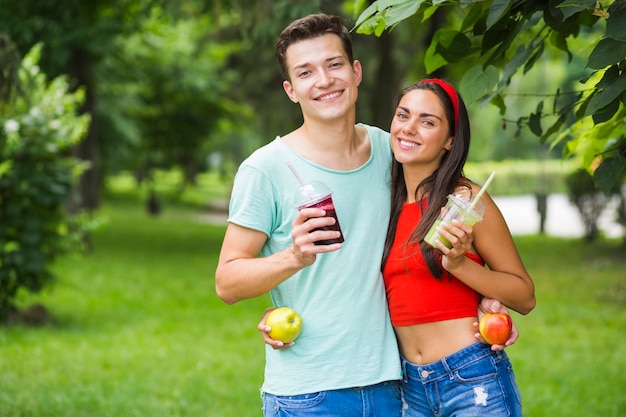 Couple standing in park holding healthy smoothies and apples