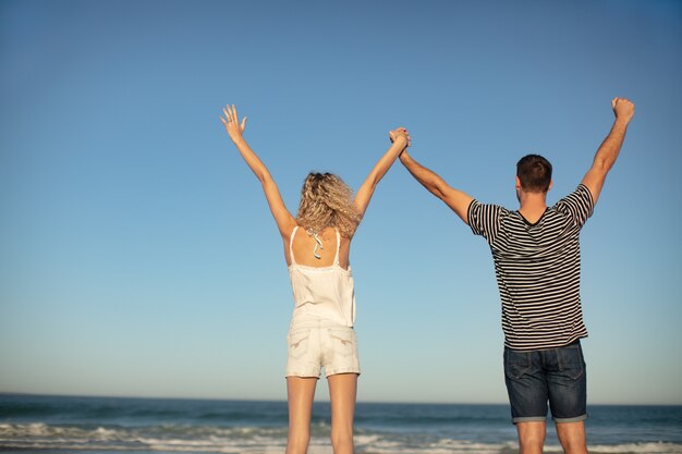 Couple standing together with arms up on the beach