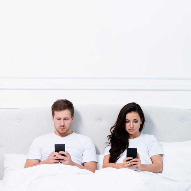 Пара, оставаясь на своих телефонах в постели