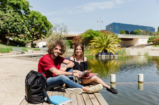 Couple of students with tablet and books in park