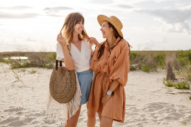 Couple of stylish girls walking and enjoying amazing coast new ocean. Straw bag, fashionable outfit.